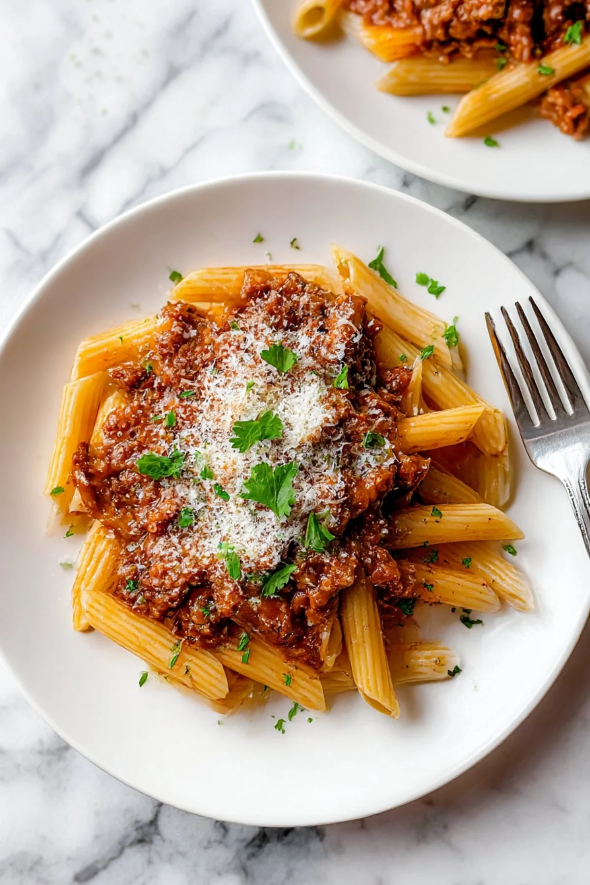 Plate of Bolognese Penne topped with fresh basil and grated cheese