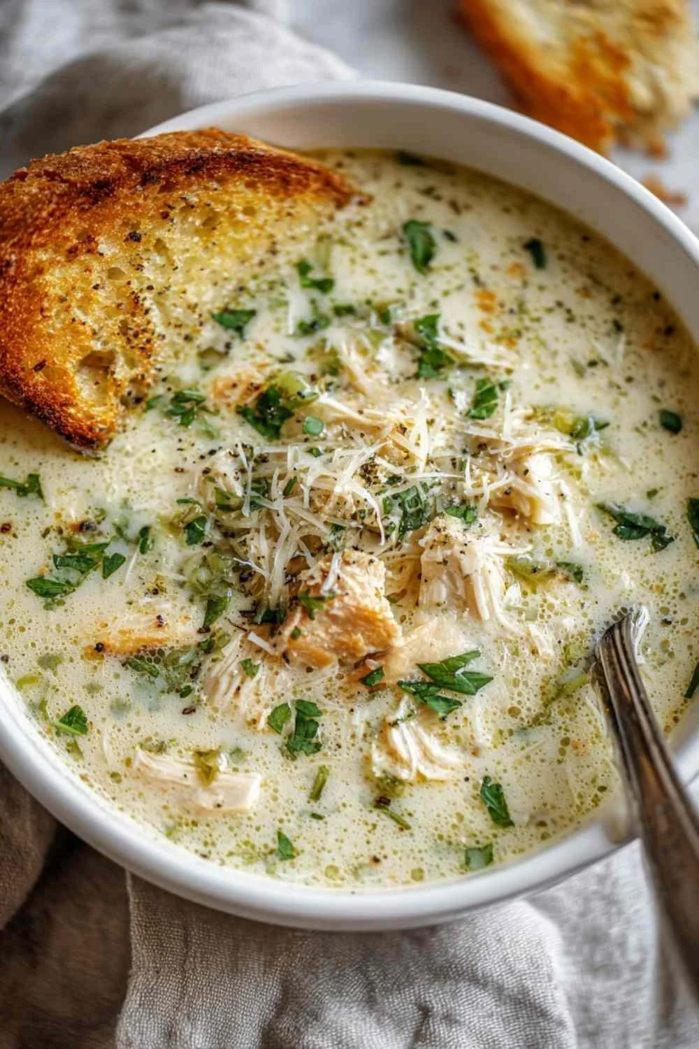 Bowl of creamy Garlic Parmesan Chicken Soup topped with herbs and croutons.