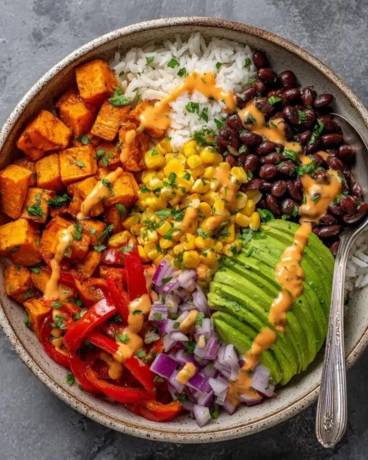 Vegan sweet potato burrito bowl with colorful veggies and toppings on a plate