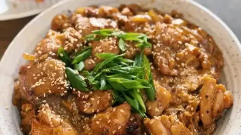 Japanese chicken and egg rice bowl garnished with green onions and served in a bowl