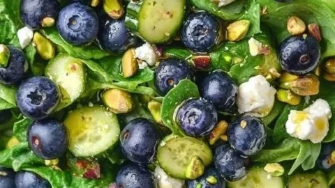 Colorful blueberry pistachio spring salad in a bowl with vibrant greens and fresh ingredients.