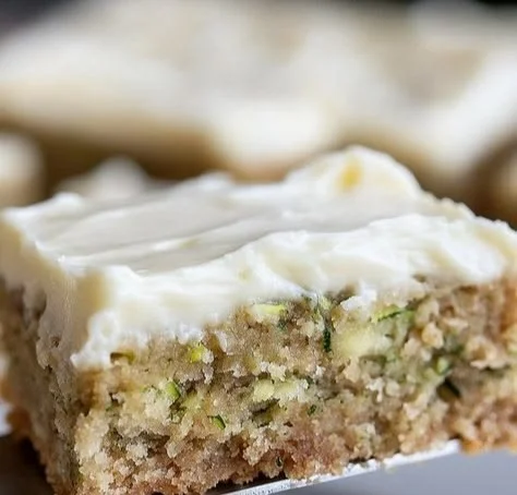 Homemade zucchini bars topped with icing on a wooden table
